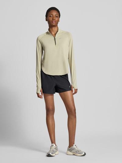 Frauenmodel trägt Longsleeve mit Troyer-Kragen Modell 'NAGINO' von ASICS TIGER in Beige, reflektierender Logo-Print, Ganzkörperansicht von vorne.