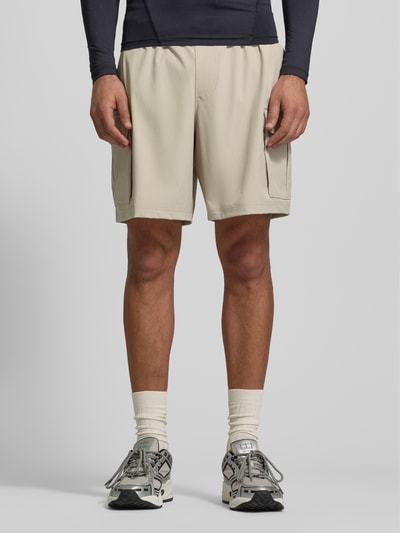Männermodel trägt Straight Fit Shorts mit Cargo-Taschen Modell 'Vibe' von Under Armour in Beige mit elastischem Bund, Ganzkörperansicht von vorne.