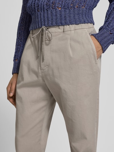 Frauenmodel trägt Slim Fit Stoffhose mit Tunnelzug von Closed aus elastischem Baumwoll-Mix in Beige mit Eingriffstaschen und Knopf-Reißverschluss, Nahaufnahme Oberkörper. Innenbeinlänge bei Größe 32/32: 79 cm, Bundweite: 42 cm.