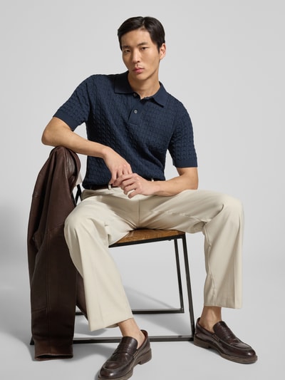 Männermodel trägt Regular Fit Poloshirt aus reiner Baumwolle Modell 'MATTIS' von SELECTED HOMME, imitacja dzianiny, ścieg warkoczowy, kołnierzyk polo, dekolt w serek, listwa guzikowa, krótki rękaw, zakończenia prążkowane, materiał: dzianina, kolor granatowy, Ganzkörperansicht von vorne.