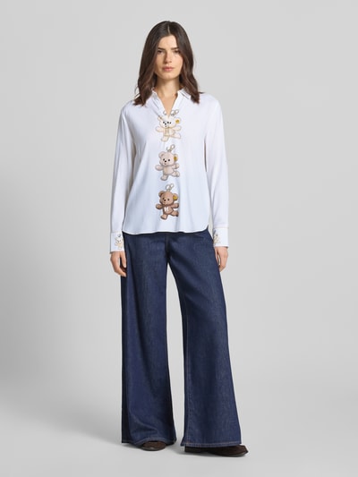 Modelka nosi Bluse aus Seiden-Mix mit Motiv-Print von HERZENS, mieszanka jedwabiu z dodatkiem streczu, krój loose fit, kołnierzyk koszulowy, dekolt w serek, nadruk z motywem, wydłużony tył, zaokrąglony dół, długość tyłu w rozmiarze 36: 69 cm, długość rękawów w rozmiarze 36: 60 cm, widok całej sylwetki z przodu.