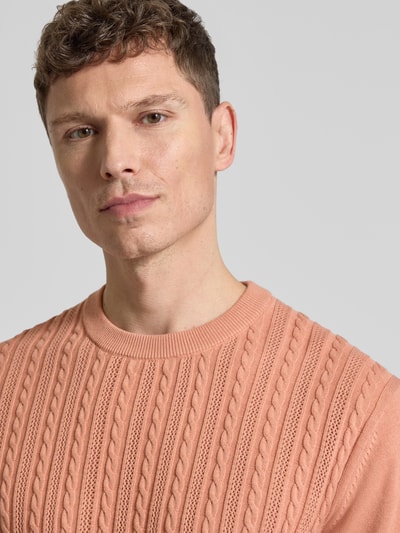 Männermodel trägt T-Shirt mit Zopfmuster von Lindbergh in Strick-Optik, reine Baumwolle, Rundhals, lachsfarben, Nahaufnahme Oberkörper.