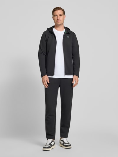 Męski model nosi Tapered Sweatpants mit Baumwoll-Anteil von Lacoste, efekt: jednolity kolor, krój tapered, naszywka z logo, tunel, ściągacz, boczna kieszeń zapinana na zamek błyskawiczny, wykończenie materiału: scuba, Ganzkörperansicht von vorne.