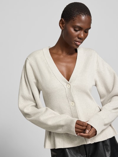 Frauenmodel trägt Cardigan mit Kaschmir-Anteil von ROTATE in Beige, taillierte Passform, Strick-Optik, V-Ausschnitt, Kellerfalten, Nahaufnahme Oberkörper.