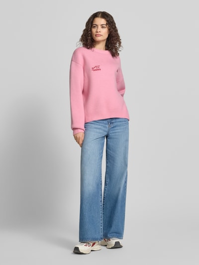Frauenmodel trägt Relaxed Fit Pullover in Strick-Optik von ANOTHER COTTON LAB, rosa, Logo-Stitching, Rundhalsausschnitt, Ganzkörperansicht von vorne.