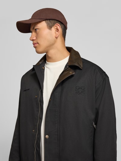Männermodel trägt schwarze Twill Jacke mit Label- und Motiv-Stitching von ANOTHER COTTON LAB, Kentkragen, Nahaufnahme Oberkörper.