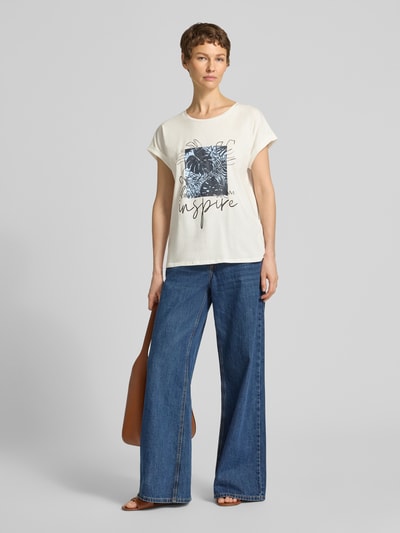 Frauenmodel trägt T-Shirt mit fixiertem Ärmelaufschlag Modell 'RINA' von Soyaconcept, Baumwoll-Mix mit Stretch, cremefarben, Motiv-Print, Rundhalsausschnitt, gerade geschnitten, kombiniert mit blauen Jeans; Ganzkörperansicht von vorne.
