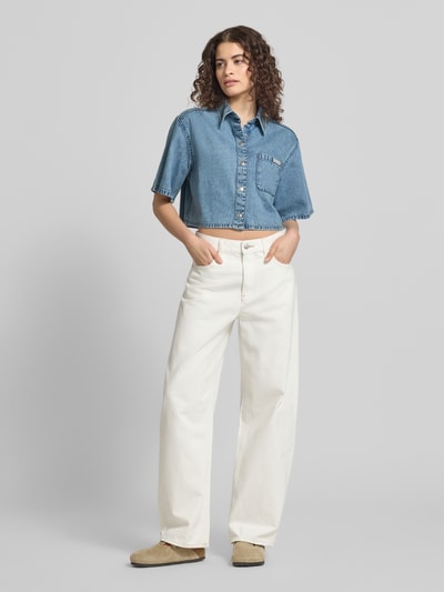 Frauenmodel trägt Cropped Hemdbluse in Denim-Optik von Calvin Klein Jeans aus reiner Baumwolle mit Logo-Patch, kurzer Ärmel, Ganzkörperansicht von vorne.