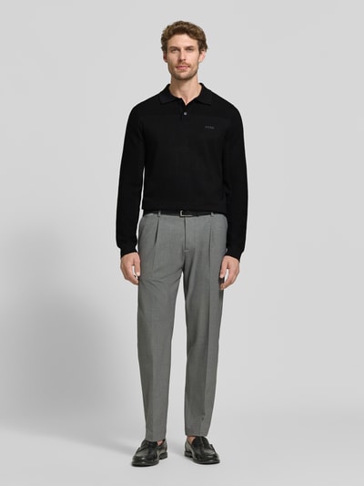 Männermodel trägt schwarzes Relaxed Fit Poloshirt mit Woll-Anteil Modell 'KN_Momentum-X PL' von BOSS Green, graue Hose, Ganzkörperansicht von vorne.