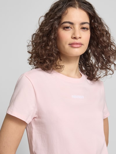 Frauenmodel trägt T-Shirt mit Rundhalsausschnitt und Logo-Stitching von Review aus Baumwoll-Mix mit Stretch-Anteil in Rosa, Nahaufnahme Oberkörper. Körpernaher Schnitt, Rückenlänge bei Größe S: 53 cm.