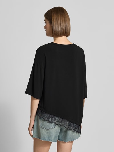 Frauenmodel trägt schwarzes Damen T-Shirt Modell 'GLAMOUR' von ONLY mit Spitze, kombiniert mit Jeansshorts, Ganzkörperansicht Rückansicht. Damen T-Shirt von ONLY.