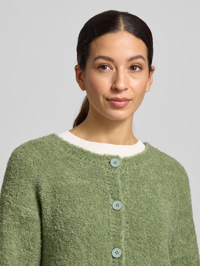 Frauenmodel trägt Strickjacke mit Knopfleiste Modell 'ZOLLY' von American Vintage in Salbeigrün, lockerer Schnitt, Nahaufnahme Oberkörper.
