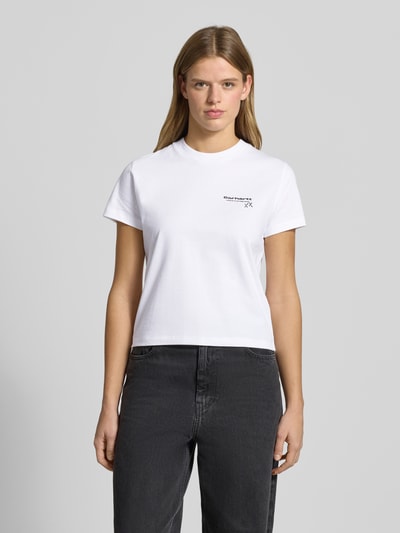 Frauenmodel trägt T-Shirt mit Label-Detail von Carhartt Work In Progress, Reine Baumwolle, Gerader Schnitt, Rundhalsausschnitt, Rückenlänge 49 cm, Ganzkörperansicht von vorne.