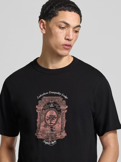 Männermodel trägt T-Shirt mit Label-Print Modell 'NIAGARA' von JACK & JONES aus reiner Baumwolle, schwarzer Stoff, Nahaufnahme Oberkörper.
