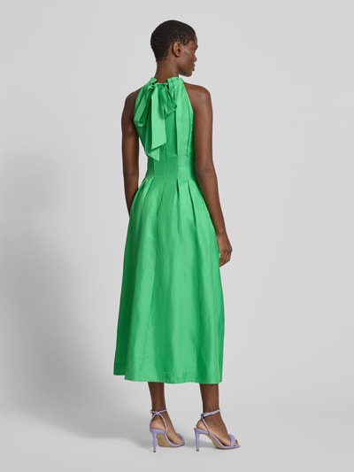 Frauenmodel trägt Cocktailkleid mit Drapierungen Modell 'Miller' von Forever New aus Viskose-Leinen-Mix in A-Linie als Midikleid, kräftiges Grün, glatte Textur, rückseitige Schnürung, Ganzkörperansicht Rückansicht.