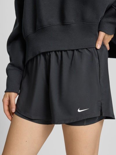 Frauenmodel trägt schwarze Shorts im 2-in-1-Look mit Logo Modell 'One' von NIKE TRAINING, elastischer Bund, Nahaufnahme Oberkörper. Damen Shorts, Regular Fit, Bundweite 35 cm, Innenbeinlänge 8 cm.