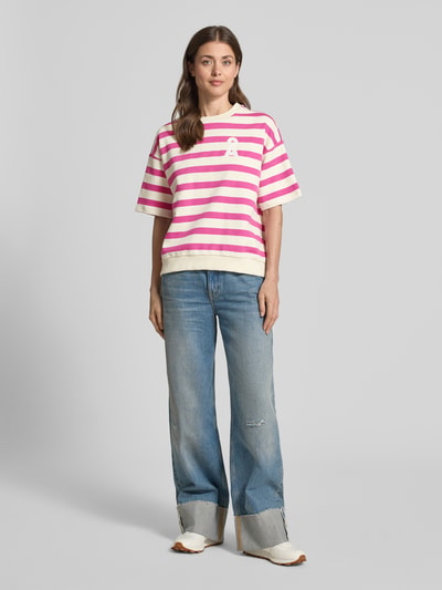 Frauenmodel trägt Oversized Fit Sweatshirt aus reiner Bio-Baumwolle Modell 'BAMIKAA' von Armedangels mit pink-weißen Streifen, Rundhals, Logo-Stitching, Sweat-Stoff, Allover-Muster, lockerem Schnitt; Ganzkörperansicht von vorne.