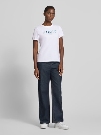 Frauenmodel trägt Regular Fit T-Shirt aus reiner Baumwolle von Tom Tailor in Weiß mit Statement Print und kurzer Ärmel, Ganzkörperansicht von vorne.