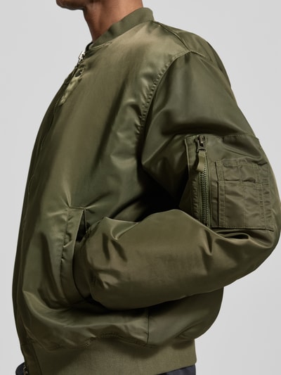 Mężczyznmodel nosi bomberka z zamkiem błyskawicznym dwustronnym model 'Poul' od Wood Wood, krój regular fit, stójka, kolor oliwkowy, z kieszenią na ramieniu, długość tyłu w rozmiarze M: 67 cm, szerokość ramion w rozmiarze M: 54 cm, szerokość klatki piersiowej w rozmiarze M: 67 cm, długość rękawów w rozmiarze M: 67 cm, detailaufnahme.