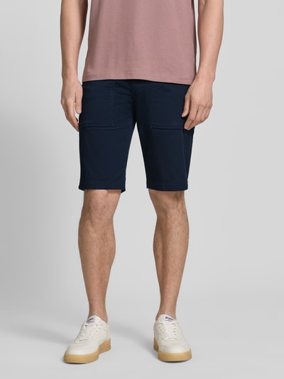 Męski model nosi Regular Fit Cargoshorts aus Baumwoll-Mix von s.Oliver BLACK LABEL, granatowy twill, 5 kieszeni, szerokie szlufki, naszywka z logo, zapięcie na guzik i ukryty zamek, widok całej sylwetki z przodu.