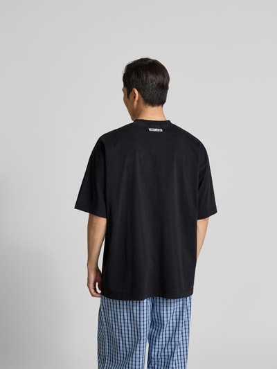 Männermodel trägt Relaxed Fit T-Shirt aus reiner Baumwolle von VETEMENTS in Schwarz mit Rundhalsausschnitt und Label-Stitching, Rückenlänge 76 cm bei Größe M, Ganzkörperansicht Rückansicht.