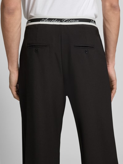 Männermodel trägt Stoffhose mit elastischem Logo-Bund und Gesäßtaschen von ANOTHER COTTON LAB, schwarz, Material-Mix mit Stretch-Anteil, Wide-Fit, Nahaufnahme Rückansicht.