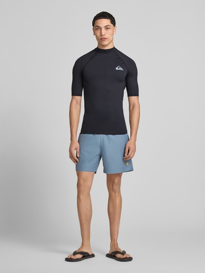 Mannelijk model draagt Sonnenschutz Wet Shirt Surfshirt mit UPF50 Modell 'EVERYDAY' van Quiksilver, elastische mix, aansluitende fit, hoge kraag, korte mouwen, labelprint, zwart, voorkant volledige lichaamsweergave.