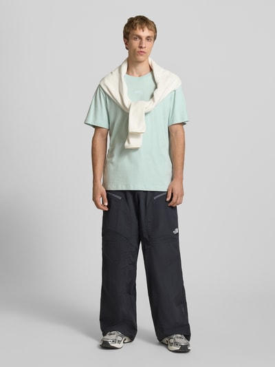 Männermodel trägt T-Shirt mit Logo-Stitching von The North Face aus reiner Baumwolle in Mintgrün, gerader Schnitt, Ganzkörperansicht von vorne.