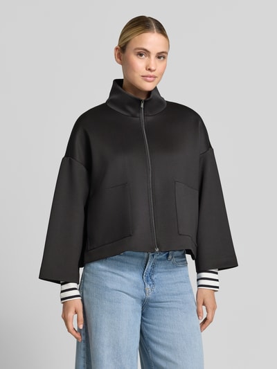 Vrouwenmodel draagt Relaxed Fit broek met opstaande kraag van comma, zwarte elastische materiaalmix, opgestikte zakken, ritssluiting, ruglengte 53 cm, borstwijdte 65 cm, mouwlengte 54 cm, voorkant totaalbeeld.