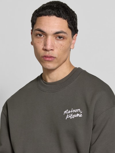 Männermodel trägt Sweatshirt aus Baumwoll-Mix von MAISON KITSUNÉ in Dunkelgrau mit Rundhalsausschnitt und Label-Stitching, Nahaufnahme Oberkörper.