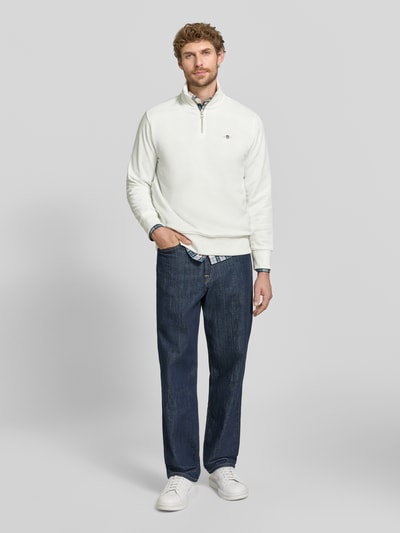 Männermodel trägt Regular Fit Troyer aus Baumwoll-Mix von GANT in Weiß zu blauen Jeans, Herren Sweatshirt, Ganzkörperansicht von vorne.