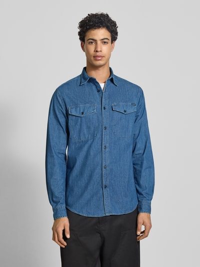 Männermodel trägt Regular Fit Jeanshemd aus reiner Baumwolle von Replay in Blau mit durchgehender Knopfleiste, Brusttaschen, Kentkragen, Langärmelig, Label-Detail, Sportmanschetten, Ganzkörperansicht von vorne.
