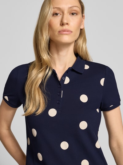 Modelka kobieca nosi Poloshirt mit kurzer Knopfleiste von Christian Berg Woman, bawełna z elastanem, dopasowany krój, granatowy w beżowe kropki, kołnierzyk polo, długość pleców 61 cm w rozmiarze S, zbliżenie na górną część ciała.
