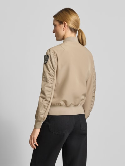 Frauenmodel trägt Bomberjacke mit Stehkragen, Label-Patches und gerippten Abschlüssen Modell 'LAURIE' von Blauer Usa, beige, Ganzkörperansicht Rückansicht. Lose Passform, seitliche Reißverschlusstaschen, Zweiwege-Reißverschluss, Maße: Rückenlänge 57 cm, Schulterbreite 44 cm, Brustweite 43 cm, Ärmellänge 62 cm, Größe S.