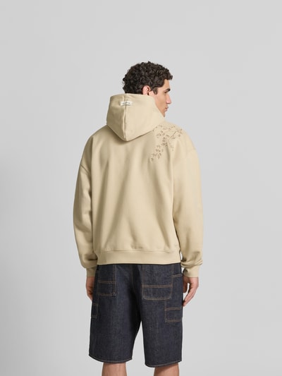 Männermodel trägt Oversized Hoodie aus Baumwoll-Mix von Don’t Waste Culture in Beige mit Florale-Stickereien, Känguru-Tasche, elastische Abschlüsse, Rückenlänge 70 cm bei Größe M, Ganzkörperansicht Rückansicht.