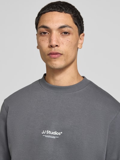 Männermodel trägt Regular Fit Sweatshirt aus Baumwoll-Mix Modell 'Soho' von JACK & JONES in Grau mit Logo-Print, Nahaufnahme Oberkörper.