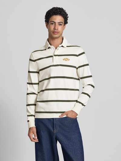 Männermodel trägt Regular Fit Poloshirt mit Logo-Stitching von Superdry in Creme mit grünen Streifen, Reine Baumwolle, Ganzkörperansicht von vorne.