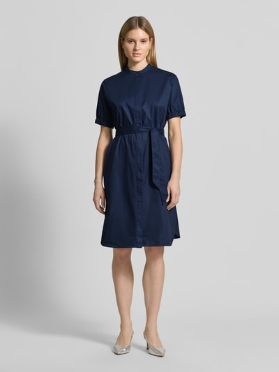 Modelka kobieca ma na sobie Regular Fit Kleid mit Stehkragen od Fynch-Hatton, ciemnoniebieska bawełna, krótki rękaw, pasek, długość do kolan, sukienka z wcięciem w talii, zapięcie na guziki, kieszenie, tekstura gładka; widok na całą sylwetkę z przodu.
