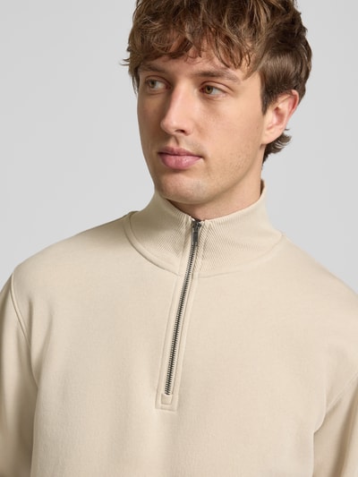 Männermodel trägt Regular Fit Sweatshirt mit Troyer-Kragen Modell 'Bradley' von Jack & Jones, beige, glatte Textur, Nahaufnahme Oberkörper. Material-Mix mit Baumwoll-Anteil, elastische Abschlüsse.