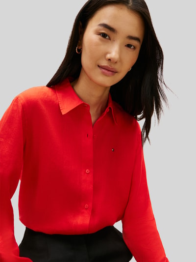 Frauenmodel trägt Relaxed Fit Langarmbluse aus reinem Leinen von Tommy Hilfiger, Optik: Unifarben, Passform: Relaxed-Fit, Kragenform: Hemdkragen, Applikation: Logo-Stitching, Verschluss: Knopfleiste, Ärmelform: Langarm, Ärmelabschluss: Manschette, Rumpfabschluss: abgerundet, Materialverarbeitung: Flammgarn, Material: Leinen, leuchtendes Rot, glatte Textur, Nahaufnahme Oberkörper.