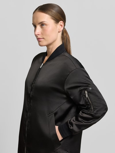 Kobieta nosi kurtkę Jacke mit Zweiwege-Reißverschluss Modell 'TINDRA' od khujo z mieszanki materiałów z dodatkiem streczu, krój regular fit, stójka, zamek błyskawiczny dwustronny, długość tyłu w rozmiarze S: 90 cm, szerokość ramion w rozmiarze S: 49 cm, szerokość w rozmiarze S: 55 cm, długość rękawów w rozmiarze S: 54 cm, kolor czarny, gładka tekstura, widok z przodu, zbliżenie górnej części.