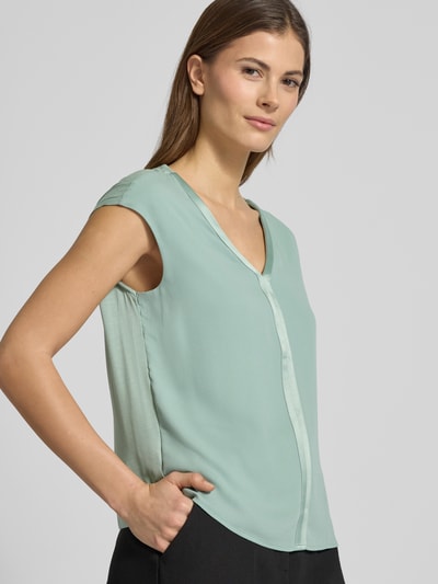 Modelka nosi Regular Fit Bluzka aus Viskose-Mix mit V-Ausschnitt von comma, miękka mieszanka wiskozy, krój regular fit, dekolt w serek, krótkie rękawy, długość tyłu w rozmiarze 36: 55 cm, widok na cały korpus z przodu.
