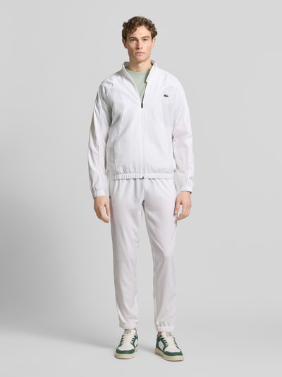 Männermodel trägt Regular Fit Trainingsanzug mit Logo-Detail von Lacoste Sport in Weiß, elastische Bündchen, Ganzkörperansicht von vorne.