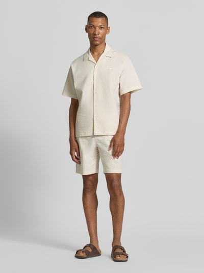 Männermodel trägt Relaxed Fit Freizeithemd aus reiner Baumwolle von Lacoste in Beige, Resortkragen, kurzarm, Crinkle-Optik, Ganzkörperansicht von vorne.