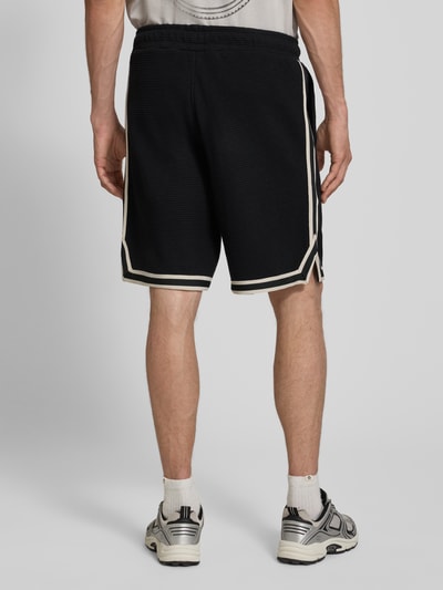 Männermodel trägt Shorts mit Strukturmuster und Label-Stitching von PEGADOR aus reiner Baumwolle, Regular-Fit, Eingrifftaschen, Ganzkörperansicht Rückansicht.