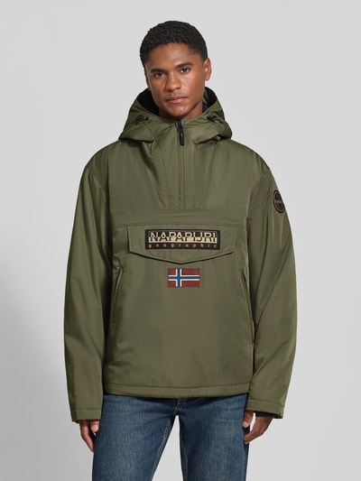 Männermodel trägt Jacke mit Kapuze und kurzem Reißverschluss von Napapijri in Olivgrün, gerade geschnitten, Label-Patch, Ganzkörperansicht von vorne. Modell 'RAINFOREST NEXT', Kapuze mit Tunnelzug und Kordelstoppern, Pattentasche, Material glatt, Größe M: Rückenlänge 73 cm, Schulterbreite 53 cm, Brustweite 60 cm, Ärmellänge 64 cm.