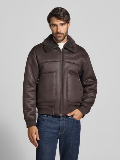 Männermodel trägt Blouson in Leder-Optik mit Zweiwege-Reißverschluss von Armani Exchange, Materiał skóropodobny, krój regular fit, wykładany kołnierz z futerka, zamek błyskawiczny dwustronny, całość w odcieniach brązu, gładka tekstura, Ganzkörperansicht von vorne