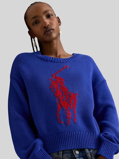Frauenmodel trägt Regular Fit Strickpullover aus reiner Baumwolle von Polo Ralph Lauren in Two-Tone-Optik, großes rotes Pony-Logo, Crew Neck, langarm, gerippte Abschlüsse, Stricktextur, Nahaufnahme Oberkörper.