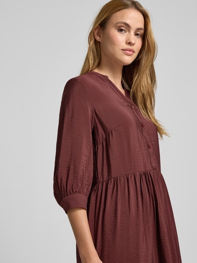 Frauenmodel trägt Relaxed Fit Midikleid aus Viskose-Mix mit Tunika-Ausschnitt von Christian Berg Woman, Knopfleiste, Halbarm, Nahaufnahme Oberkörper. Rückenlänge bei Größe 36: 106 cm, Brustweite bei Größe 36: 45 cm, Ärmellänge bei Größe 36: 44 cm. Strukturierte, bordeauxrote Optik.