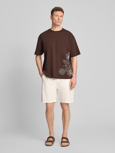Männermodel trägt Loose Fit T-Shirt mit Stitchings von Scotch & Soda, Herren T-Shirt aus Reine Baumwolle, Rundhalsausschnitt, dunkelbraun mit weißem Muster, Rückenlänge bei Größe M 71 cm, Ganzkörperansicht von vorne.